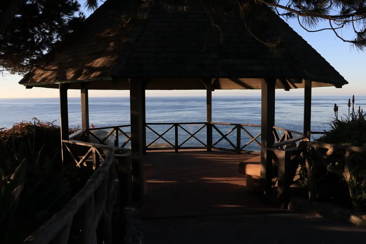 The wooden gazebo at Heisler Park, its rustic railing and shingled roof framing a calm blue ocean and the horizon beyond.
