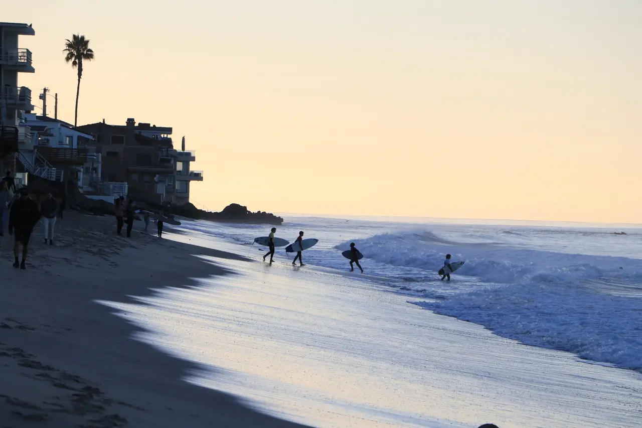 Silhouetted figures heading down to the water at dusk along a Laguna beach, the wet sand reflecting a golden sky.