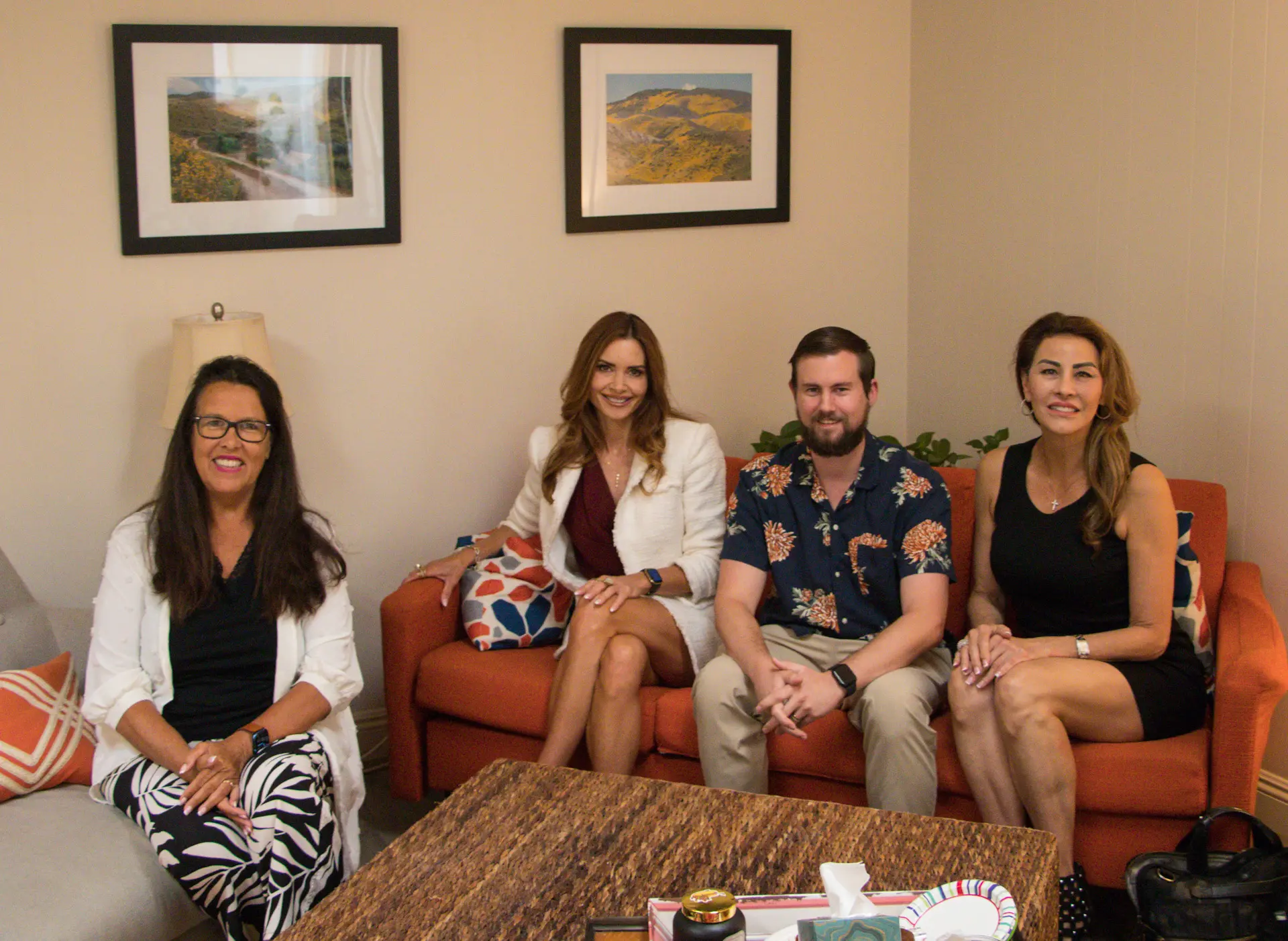 Four therapists from Laguna Beach Counseling seated together on the orange sofa and armchair in the practice's office.